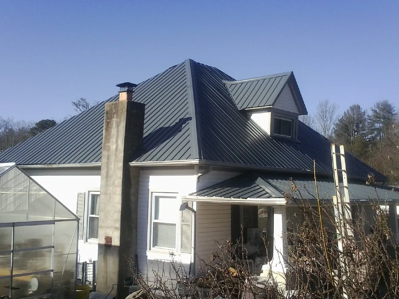 Dark blue standing seam metal roof on a white farmhouse with dormer — Slate & Tile Roof Repair by Roofing Brothers in Estill