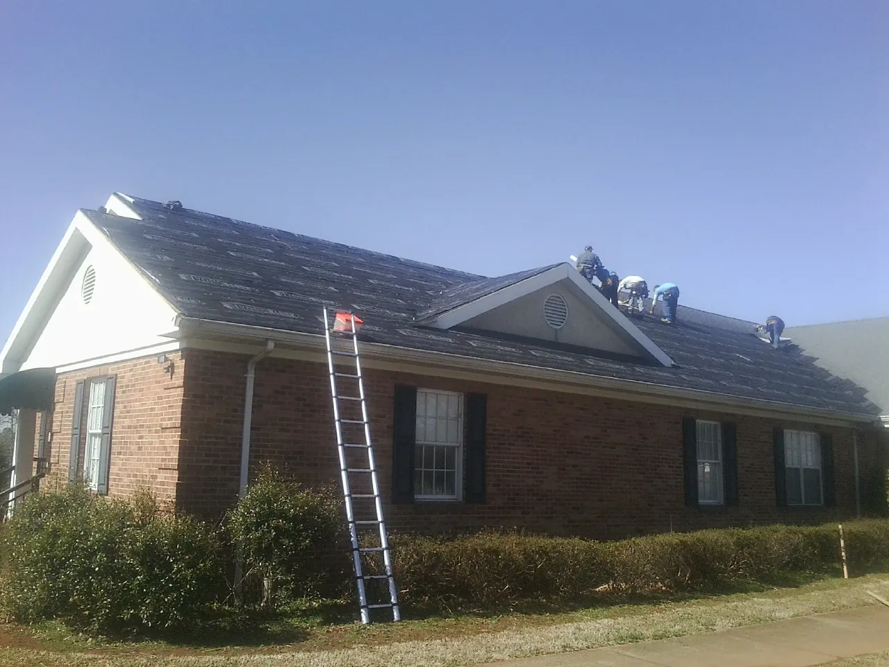 Crew tearing shingles off a brick ranch roof with a ladder set — Emergency Roof Repair work by our crew in Estill