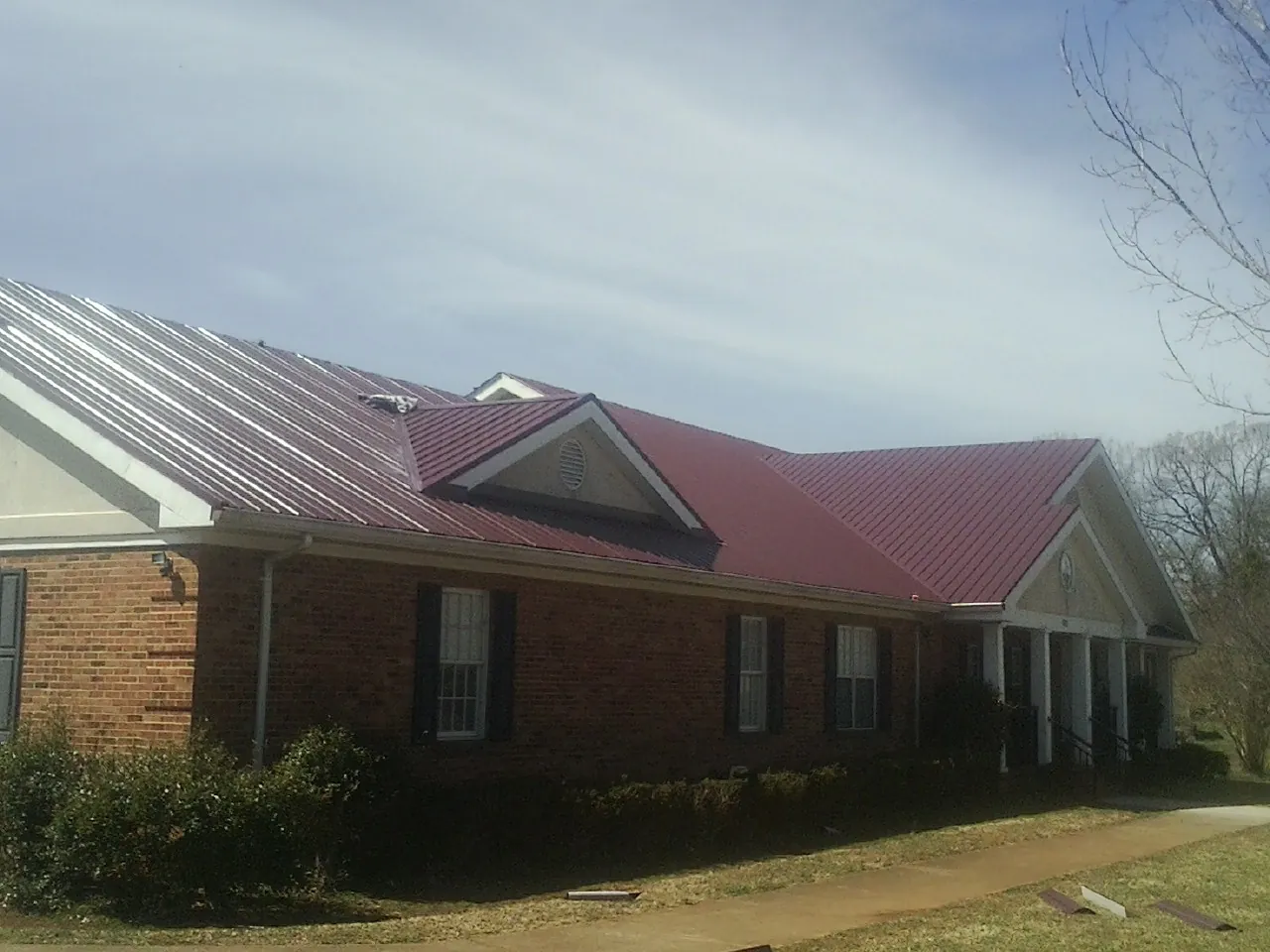 Red metal roof with gabled entries on a long brick building, from a Hail Damage Roof Repair job in Estill
