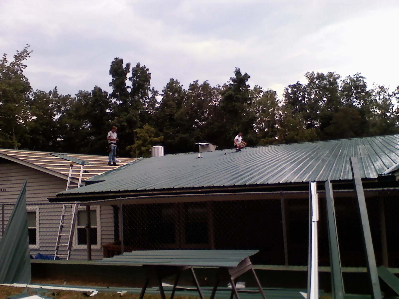 Two roofers installing green metal panels above a covered porch in Estill