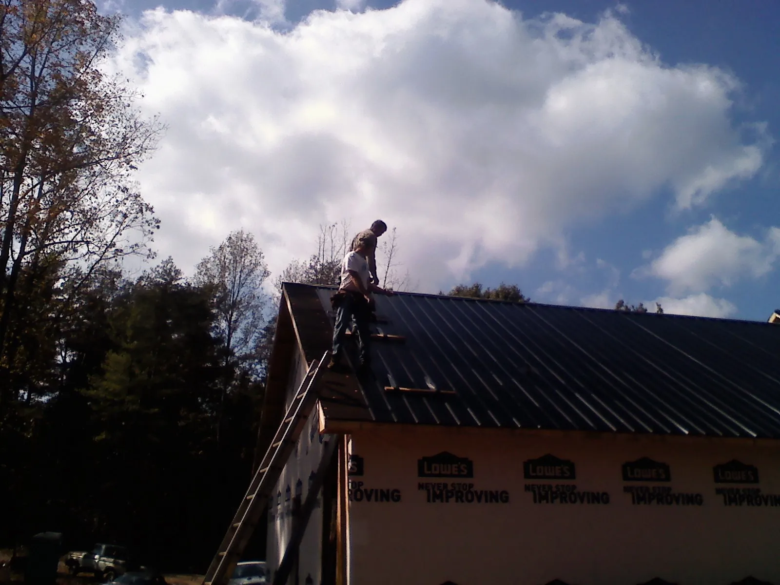 Roofer fastening dark metal panels high against a cloudy sky, from a Roof Inspection job in Estill